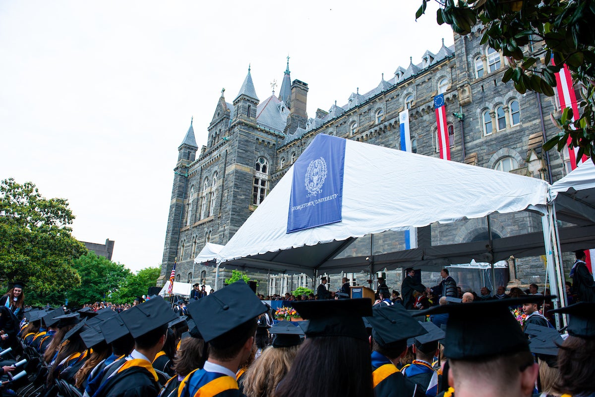 Students in caps and gowns watch commencement in front of Healy Hall.