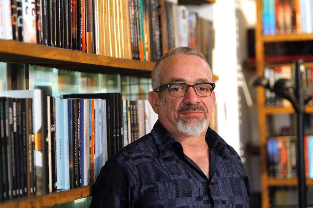 Author Rabih Alameddine stands in front of a bookcase.