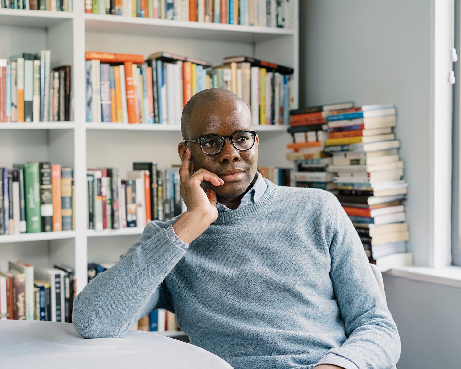 Tope Folarin leans on a table with a bookshelf in the background.