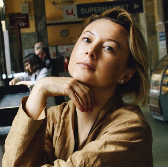 Valzhyna Mort in yellow blouse with hand resting on her chin.